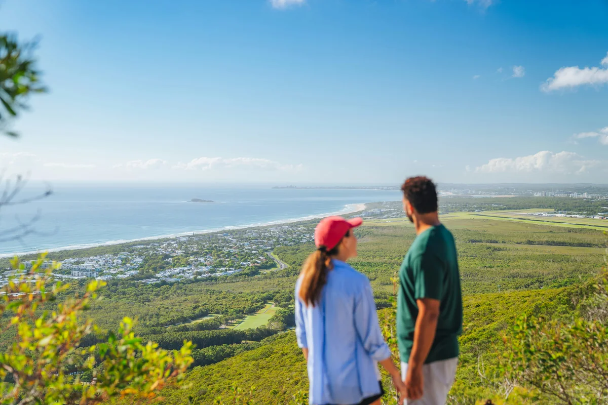Two people overlooking a coastal community from a high green hillside