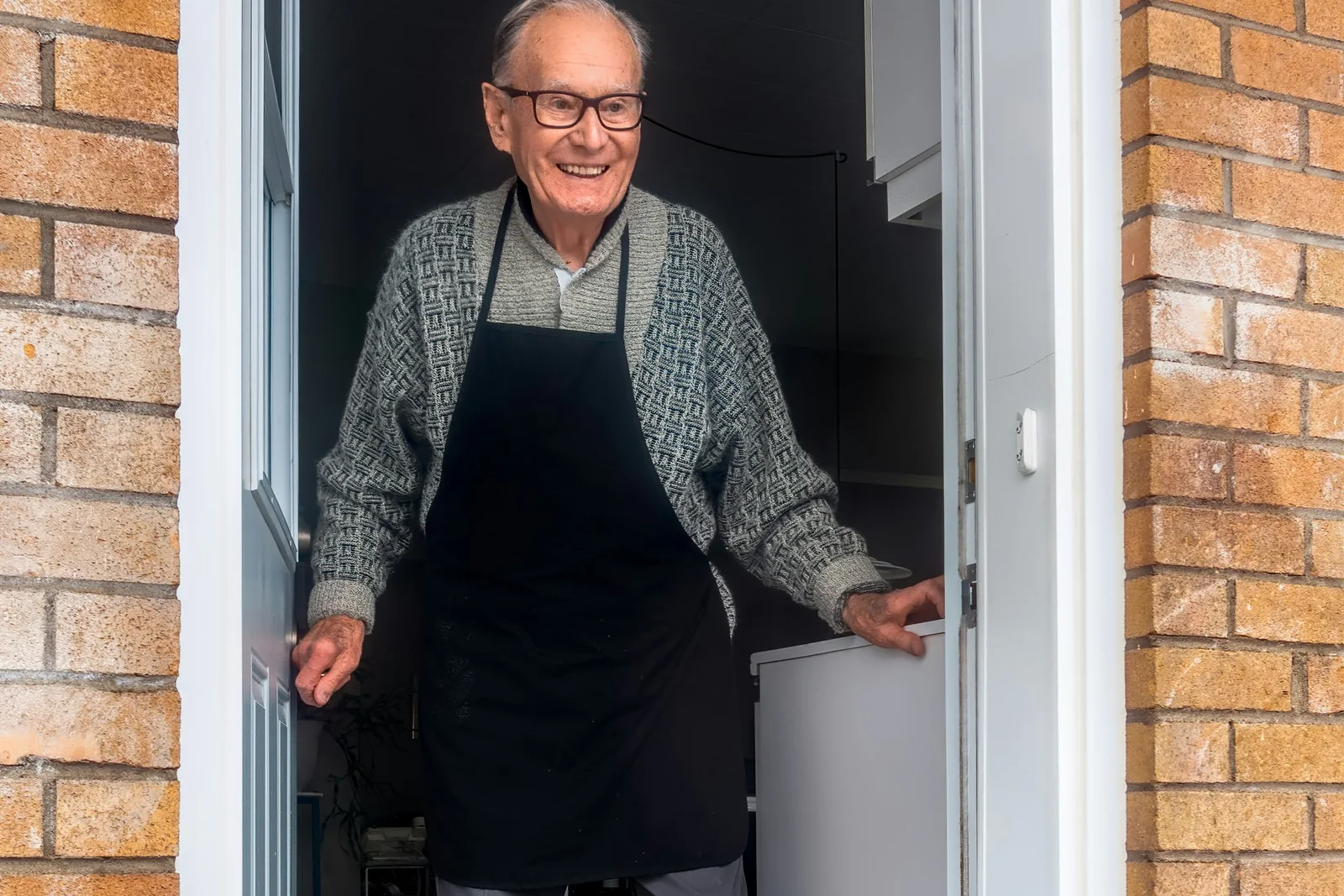 A smiling older man standing in the open doorway of his home