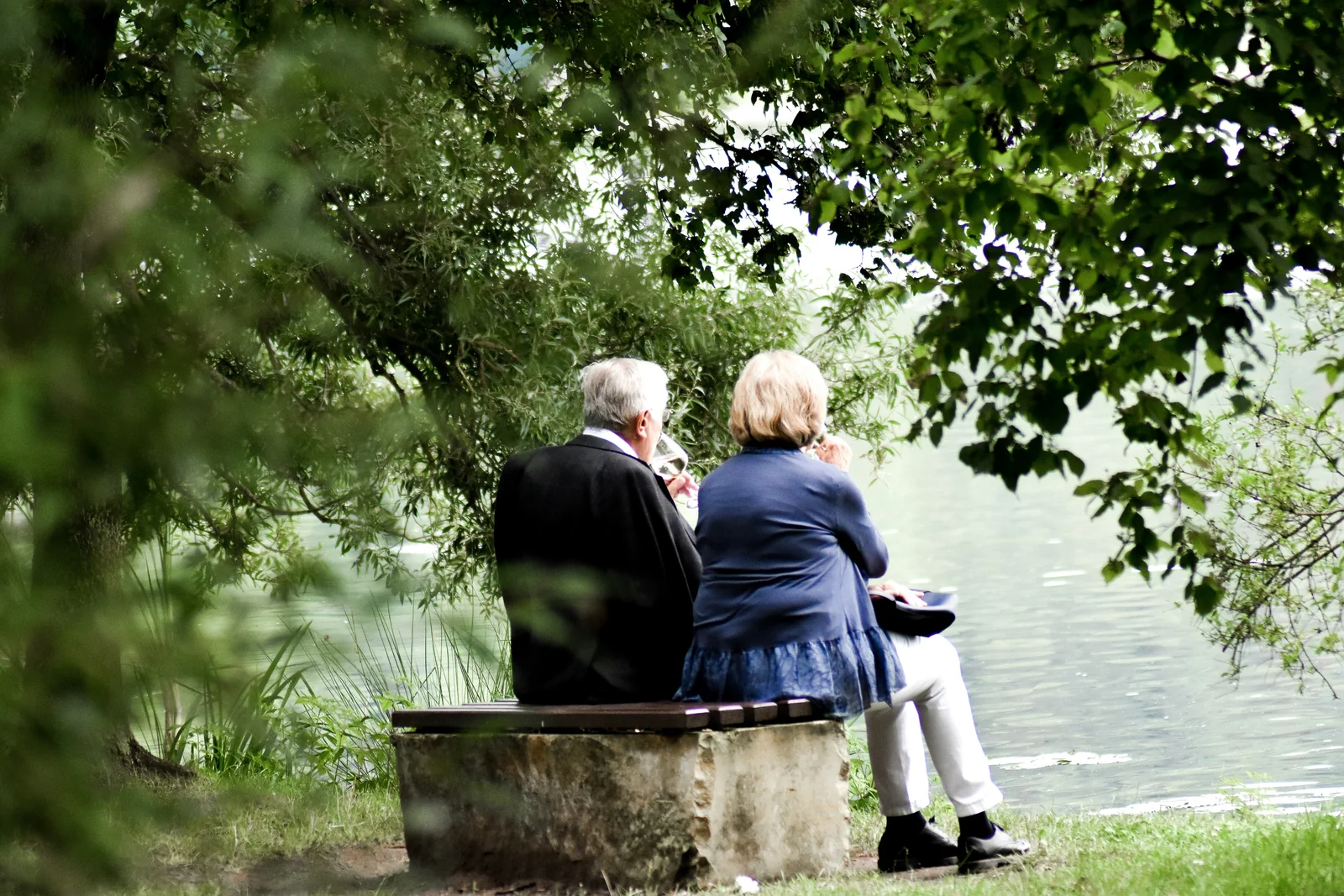 An older couple sitting together beside a quiet lake