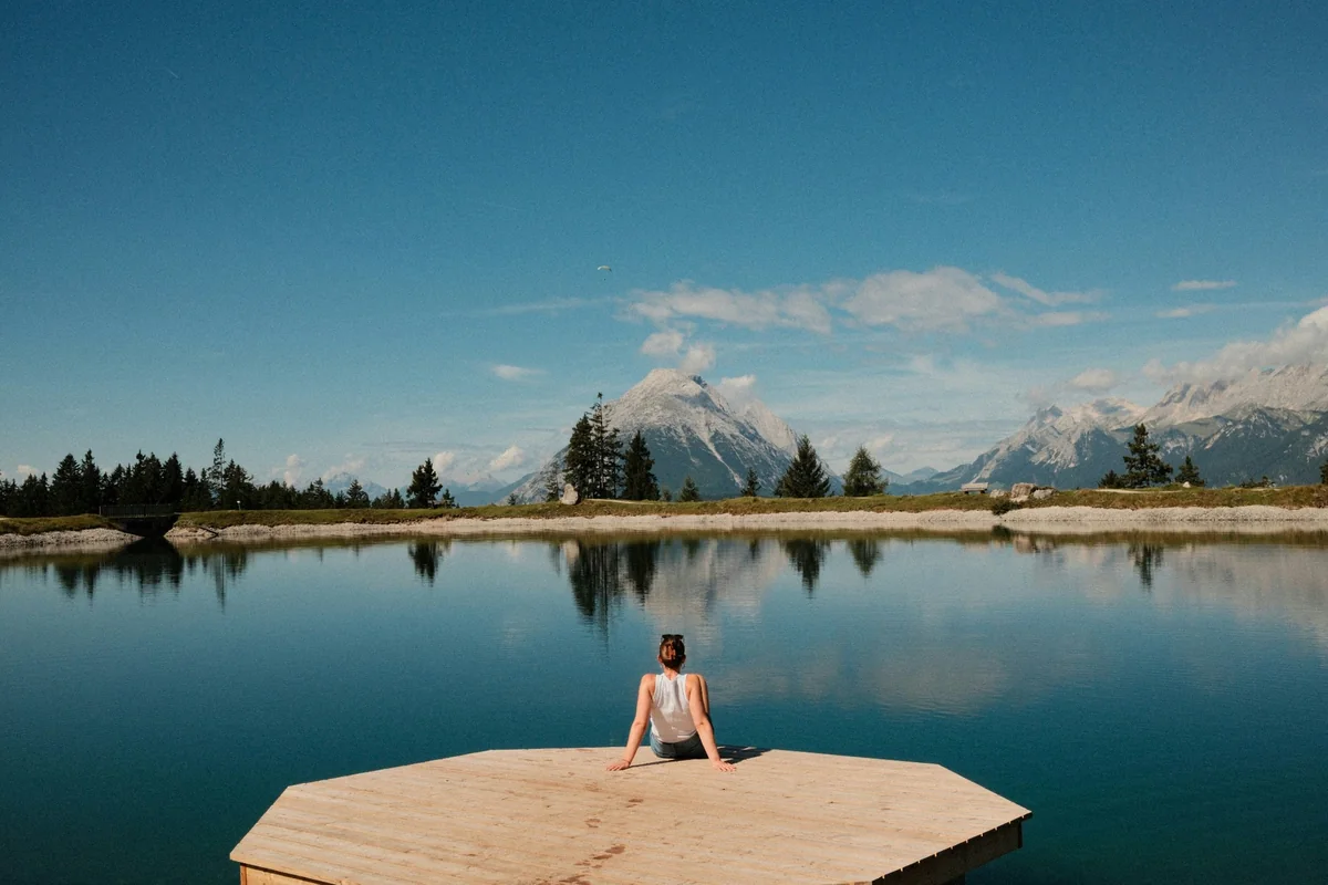 A person sitting alone beside a still mountain lake